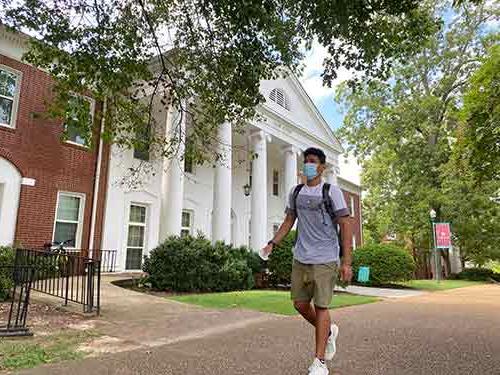 A student wearing a mask walks in front of Pitts Hall