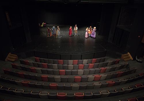 Wide shot of Price Theater interior with stage and front rows of seating, while students rehearse on stage